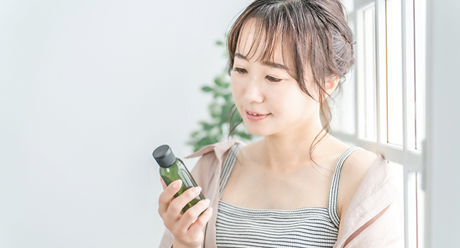 化粧品のボトルを手に持って見る女性の写真